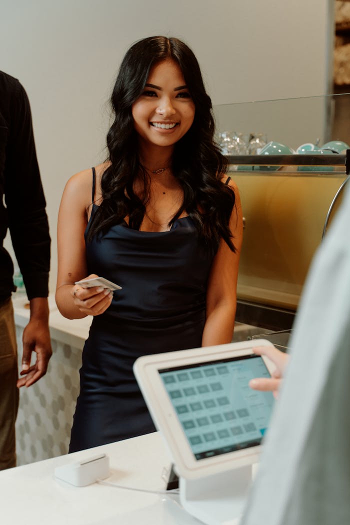 about-us A woman in a black dress smiling while making a cashless payment at a store.